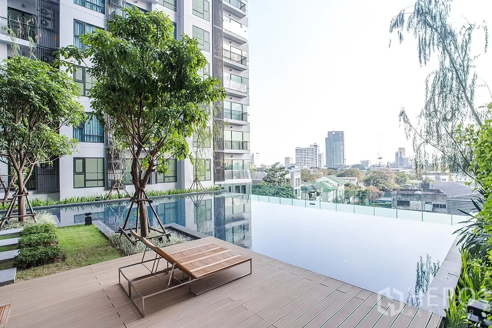 Condominium for rent or sale in Khlong Toei, Bangkok - Infinity-edge swimming pool with timber deck, sun lounger and lush trees overlooking the Bangkok skyline.