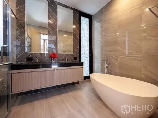 Detached House for sale in Prawet, Bangkok - Elegant bathroom with freestanding bathtub, twin sinks, and marble-style wall tiles.