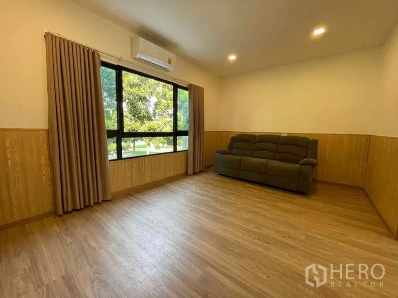 Townhouse for rent or sale in Bang Kapi, Bangkok - Living area with wide window overlooking greenery and wood panel wainscoting.