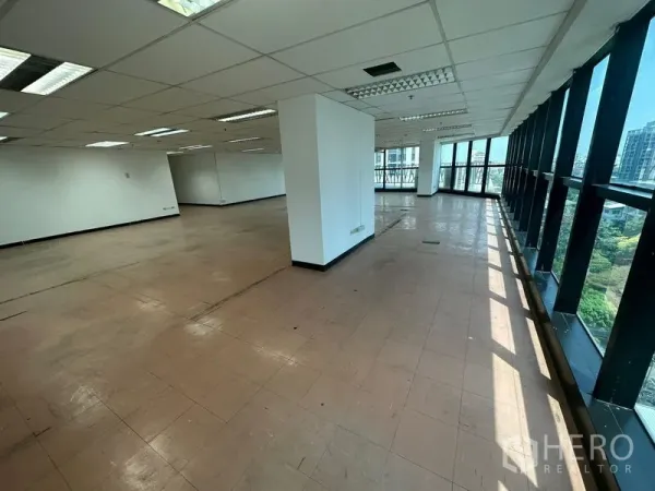 Office Space for rent - Bright office area with a long wall of windows, central column, and daylight across tiled floors.