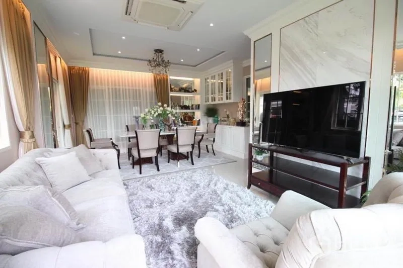 Detached House for rent or sale in Lat Phrao, Bangkok - Bright open-plan living and dining area with chandelier, large TV and plush rug.