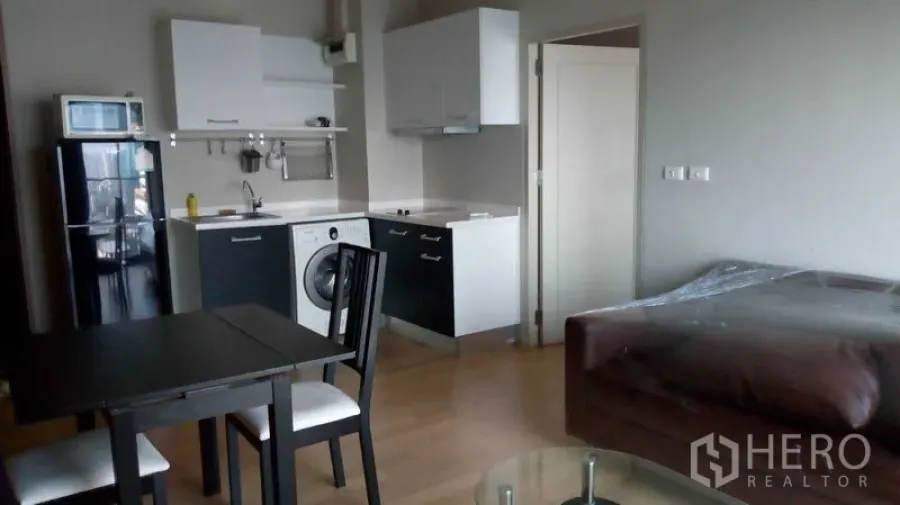 Condominium for rent in Watthana, Bangkok - Compact kitchen with refrigerator, microwave, washing machine and dining set beside a sofa in an Ekkamai condo.