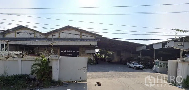 Factory for rent in Mueang Samut Prakan, Samut Prakan - Front view of a gated industrial warehouse complex with wide driveway and metal roofing in Samut Prakan.