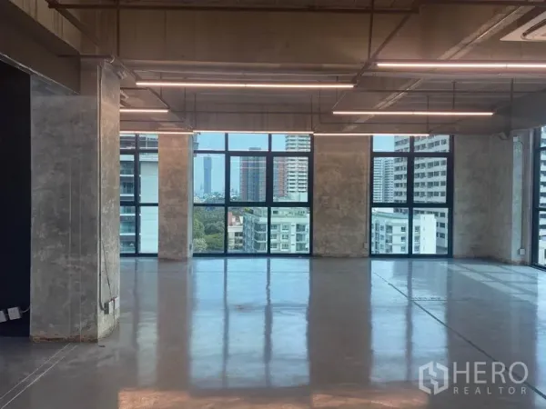 办公空间 出租在Khlong Toei, Bangkok - 开放式办公楼层，裸顶与长条LED灯，通过大窗可见曼谷天际线。