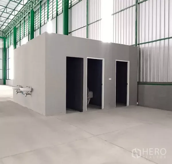 Warehouse for rent in Bang Bon, Bangkok - Warehouse interior with restroom block, smooth concrete floor, green steel columns and ventilated wall panels.