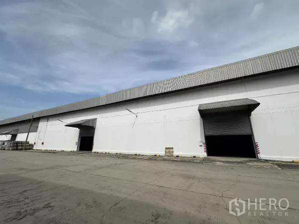 Warehouse for rent in Phra Nakhon Si Ayutthaya - Long warehouse exterior with multiple canopy-covered loading bays and a wide truck maneuvering yard.