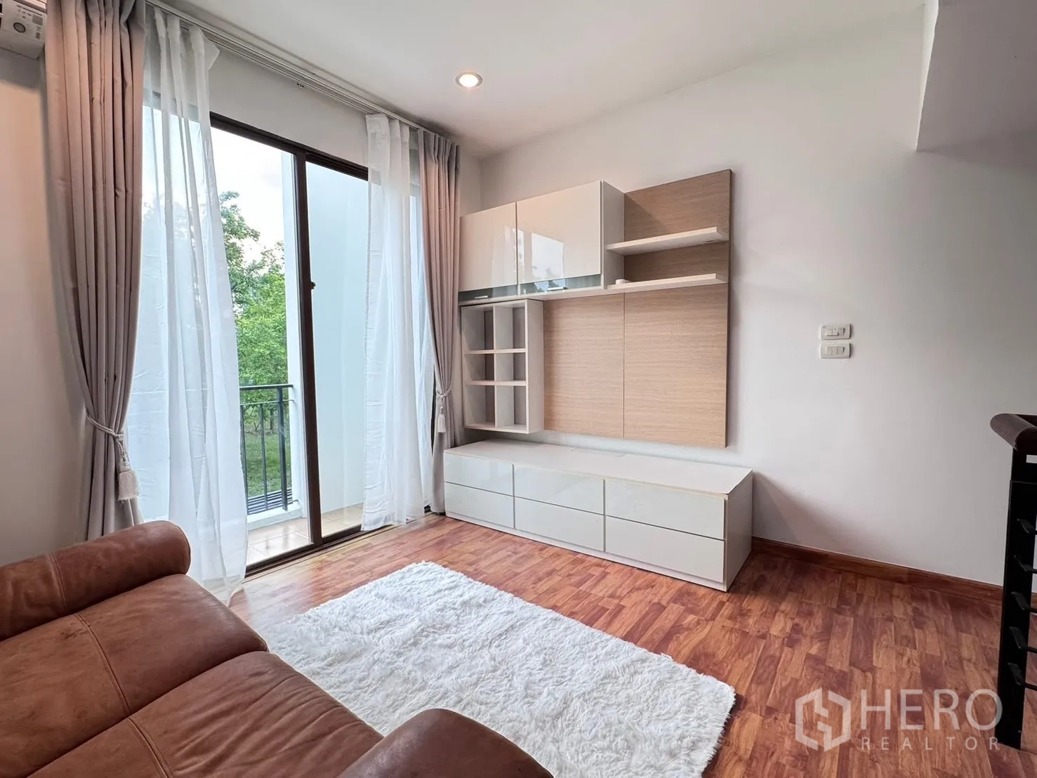 Townhouse for rent in Phra Khanong, Bangkok - Living area with sofa, rug, wall cabinet, and balcony doors.