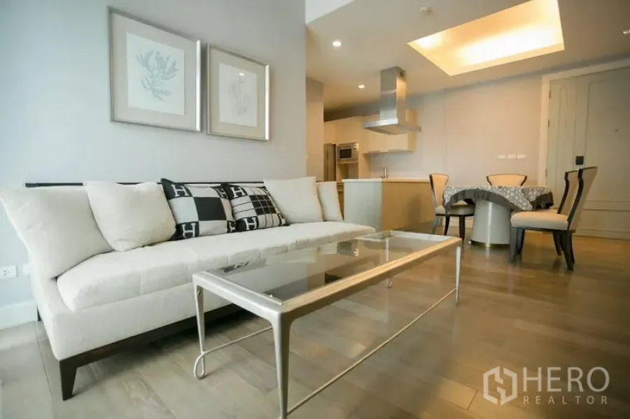 Condominium for rent in Pathum Wan, Bangkok - Bright open-plan living room with cream sofa, glass coffee table, wood floors and adjoining kitchen with dining area.