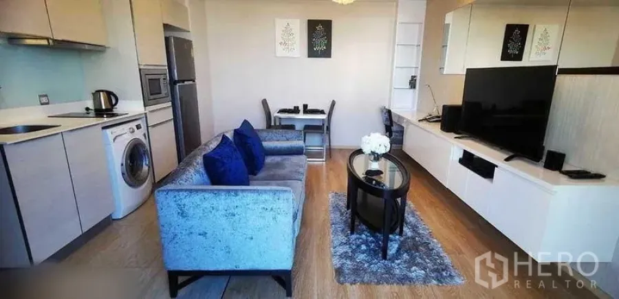 Condominium for rent in Watthana, Bangkok - Open living, dining and kitchen area with built-in media wall and gray sofa.