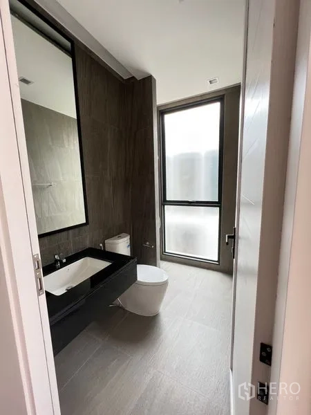 Home Office for sale in Wang Thonglang, Bangkok - Modern bathroom with large frosted window, wall-hung toilet, and long black vanity.