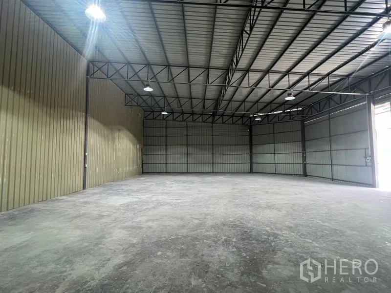 Warehouse for rent in Phra Khanong, Bangkok - Interior view toward the entrance highlighting the high ceiling and gray metal walls for storage.