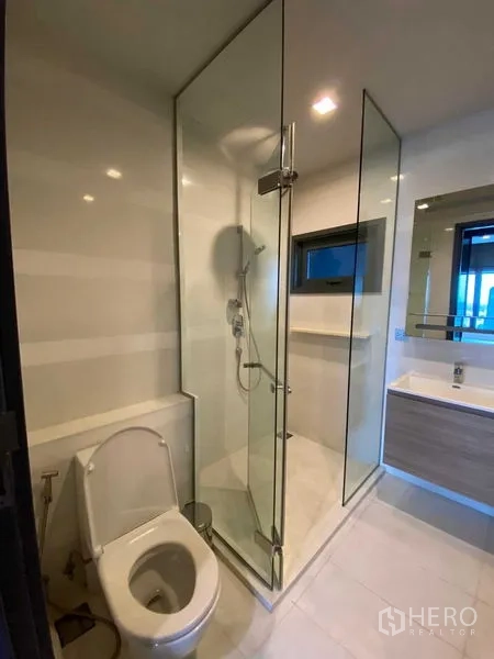 Condominium for rent in Khlong Toei, Bangkok - Modern bathroom with glass-enclosed shower, toilet and vanity.