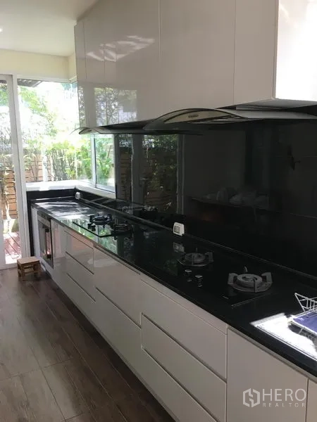 Townhouse for sale in Huai Khwang, Bangkok - Modern linear kitchen with black granite countertops, gas hobs and garden-view windows.