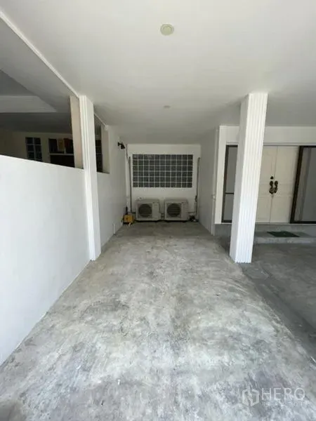 Townhouse for rent in Phra Khanong, Bangkok - Covered carport with concrete floor and air-conditioning units at the front of the townhouse.
