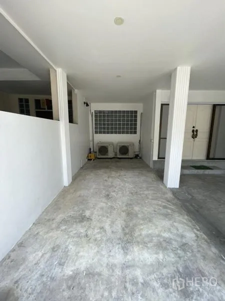 Townhouse for rent in Phra Khanong, Bangkok - Covered carport with concrete floor and air-conditioning units at the front of the townhouse.