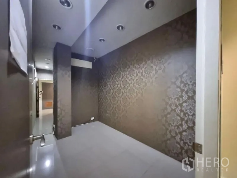 Shophouse for rent in Watthana, Bangkok - Narrow room with dark damask wallpaper and downlights, suitable for a private consultation space.