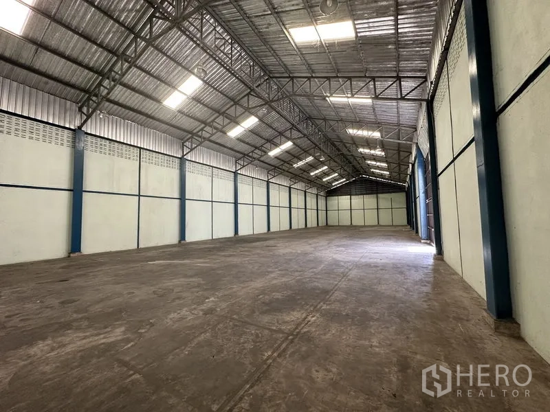 Warehouse for rent in Phra Nakhon Si Ayutthaya - Long clear-span storage hall with insulated roofing, bright lighting, and a wide sliding door entry.