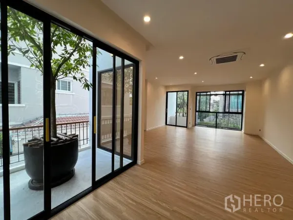 Home Office for sale in Phra Khanong, Bangkok - Open‑plan room with wood floors, sliding glass doors and a balcony planter with a tree.