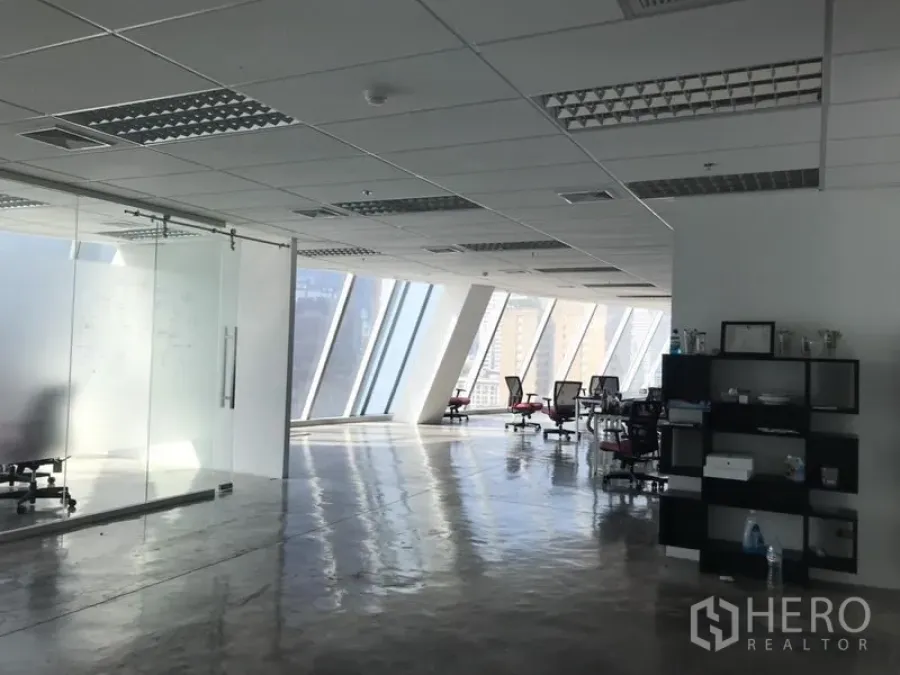 Office Space for rent in Khlong Toei, Bangkok - Bright office floor with angled façade windows, glass‑walled meeting room and desks overlooking the skyline.