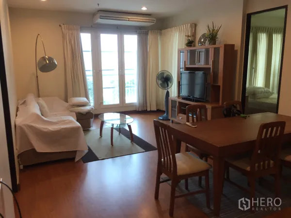 Condominium for rent in Khlong Toei, Bangkok - Living room with sofa, TV unit, dining table and balcony doors with curtains.