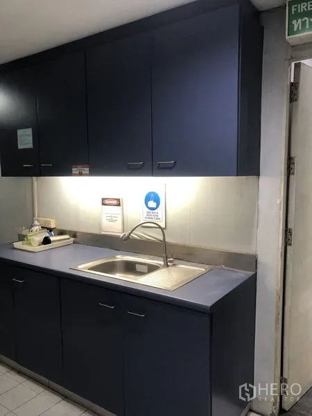 Office Space for rent - Compact pantry with sink, under-cabinet lighting, and dark blue cabinetry.