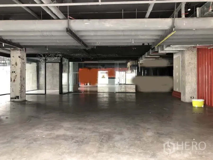 Retail Space for rent in Khlong Toei, Bangkok - Open-plan commercial space with high ceiling, large glass storefronts, and industrial-style piping.