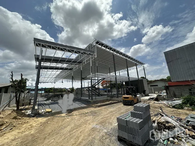 Warehouse for rent in Lat Krabang, Bangkok - Front elevation of a partially roofed warehouse with a forklift and stacked materials on site.
