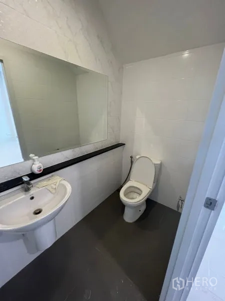 Home Office for rent - Guest restroom with long mirror, white sink, and toilet on grey tile flooring.