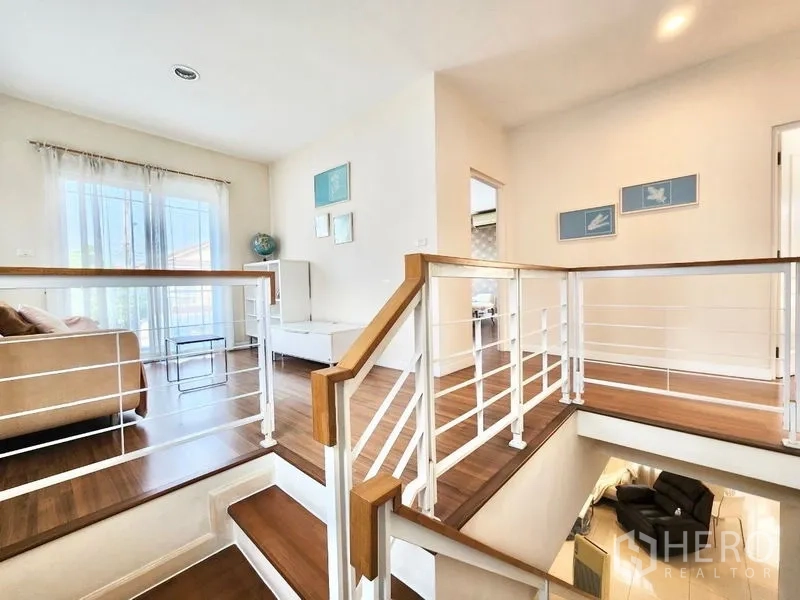 Detached House for rent in Prawet, Bangkok - Staircase and upper landing with wood floors, white railing and abundant natural light.