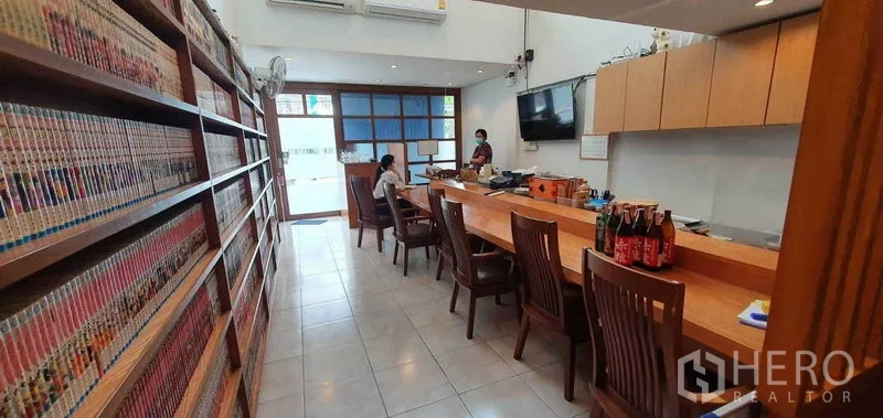 店屋 出租在Khlong Toei, Bangkok - 前厅就餐区，长木吧台、整墙书架与地砖