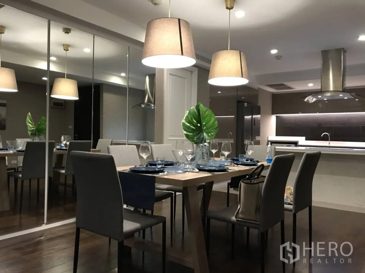 Condominium for rent or sale in Pathum Wan, Bangkok - Elegant open-plan dining area with mirrored wall, pendant lights, and view to a modern kitchen in a Bangkok condo.