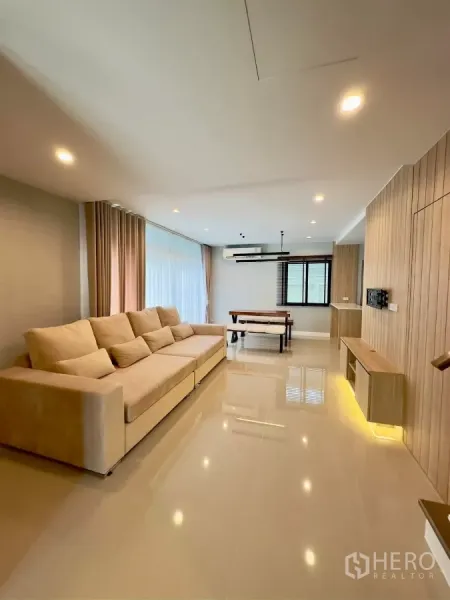 Detached House for rent in Samut Prakan - Spacious living room with long sofa, floor-to-ceiling curtains and a dining table.