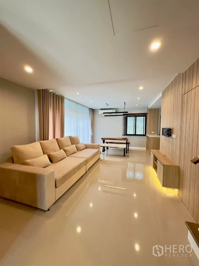 Detached House for rent in Samut Prakan - Spacious living room with long sofa, floor-to-ceiling curtains and a dining table.