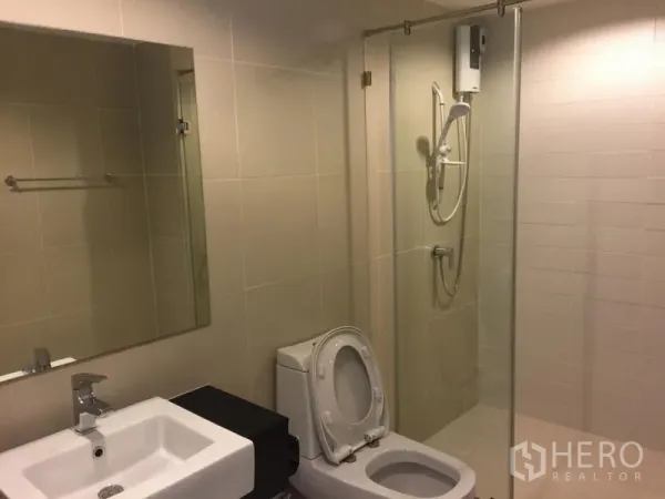 Condominium for rent in Huai Khwang, Bangkok - Modern bathroom with glass-enclosed shower, water heater, toilet and vanity.