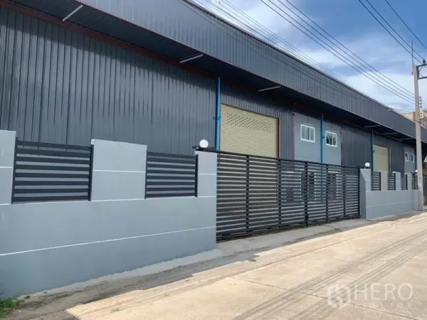 工厂 出租在Khlong Luang, Pathum Thani - 现代化工厂外立面，灰色金属板、卷闸门与围栏，临宽阔街道。