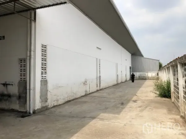 Factory for rent in Nonthaburi - Wide concrete side yard running along the factory beside a perimeter wall.