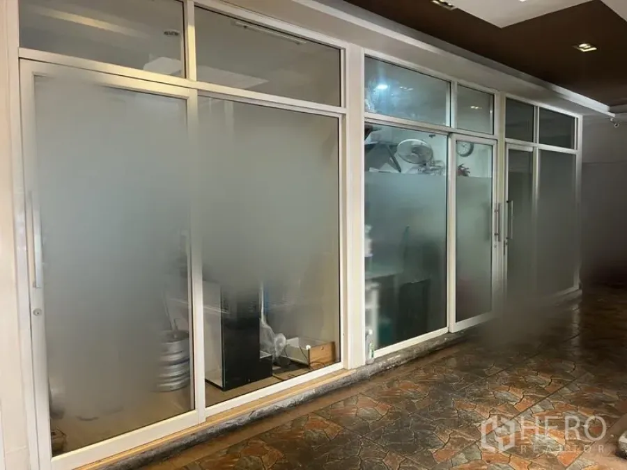 Retail Space for rent in Khlong Toei, Bangkok - Frosted-glass shopfront with white aluminum frames and a sliding door along a covered tiled walkway.
