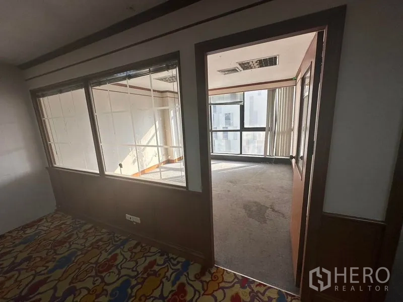 Office Space for rent - Private office with large windows and vertical blinds, connected to the main area via a glass partition and wooden door.