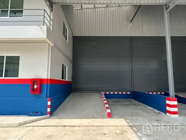 Warehouse for rent in Samut Prakan - Close view of covered loading bay with roller shutter door, ramp guides and a wall‑mounted fire hose cabinet.
