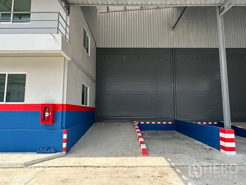 Warehouse for rent in Samut Prakan - Close view of covered loading bay with roller shutter door, ramp guides and a wall‑mounted fire hose cabinet.