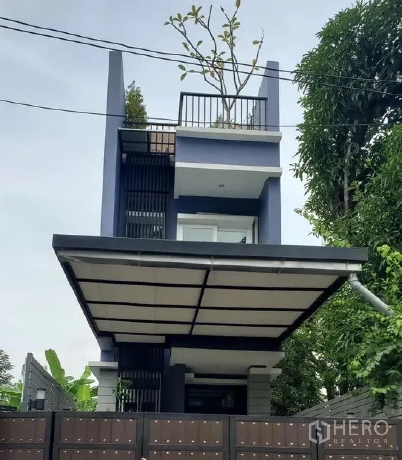 Detached House for rent in Watthana, Bangkok - Contemporary three-storey detached house with rooftop terrace, covered carport and gated entrance amid mature trees.