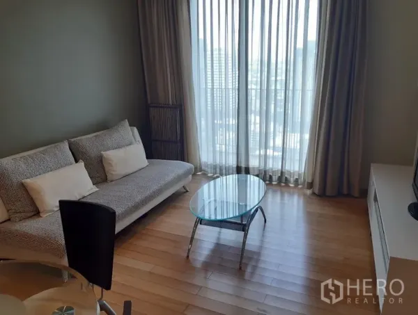 Condominium for rent in Khlong Toei, Bangkok - Bright living room with sofa, glass coffee table and floor-to-ceiling windows opening to a balcony.
