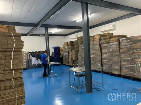 Warehouse for rent in Bang Kapi, Bangkok - Spacious storage zone with blue floor, palletized boxes, fluorescent lighting and steel supports.