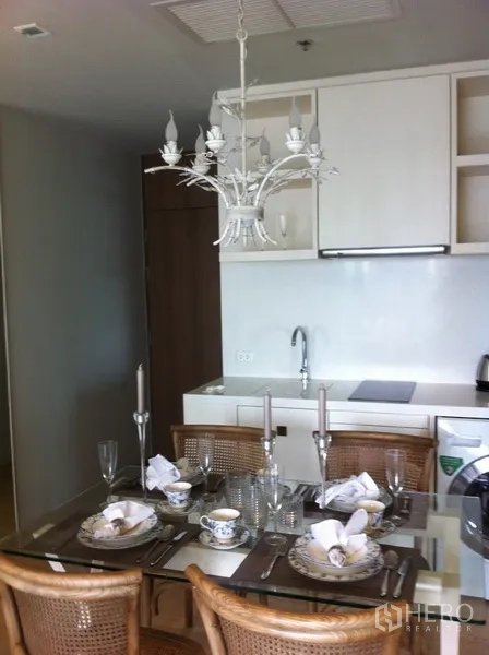 Condominium for rent in Bangkok - Glass-top dining table set for four beneath a decorative chandelier.
