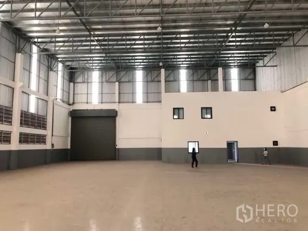 Factory for rent or sale in Samut Prakan - Warehouse interior showing large roller shutter door and attached office block.