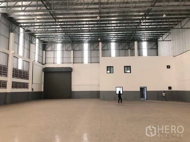 Factory for rent or sale in Samut Prakan - Warehouse interior showing large roller shutter door and attached office block.