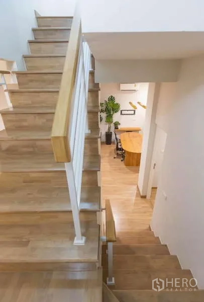 Detached House for rent or sale in Lat Phrao, Bangkok - Wood staircase with white railing looking down to the open-plan living area.