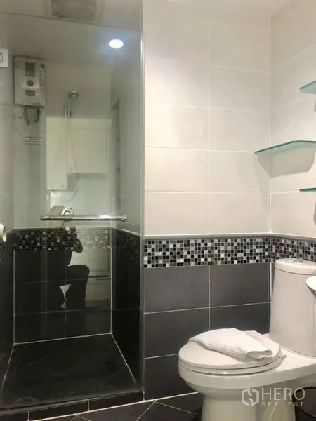 Condominium for rent in Khlong Toei, Bangkok - Modern bathroom with glass-enclosed shower, mosaic tile trim and floating shelves.
