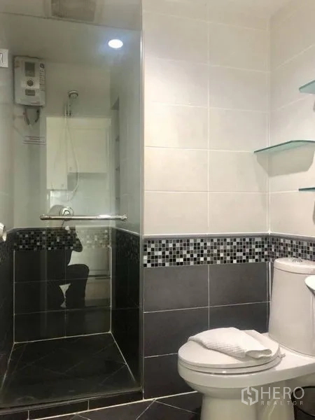 Condominium for rent in Khlong Toei, Bangkok - Modern bathroom with glass-enclosed shower, mosaic tile trim and floating shelves.