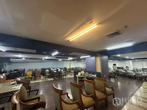 Retail Space for rent - Wide retail floor featuring seating displays under a dropped ceiling with warm lighting.